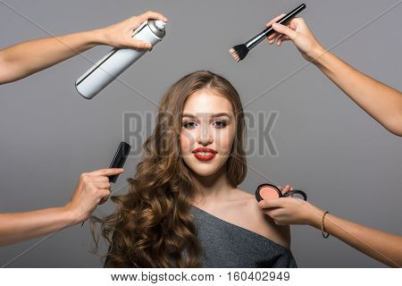 Makeup and hairstyle process, portrait of beautiful young woman and many hands with a brush, powder, comb and hairspray. Studio shot