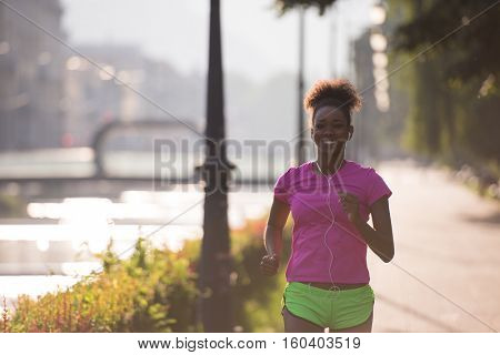 Beautiful young sporty african american woman running at early morning jogging with city sunrise scene in background