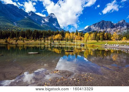 The shallow lake among the woods and mountains. Concept of autotourism and hiking. Shining day in Canmore, Canadian Rockies