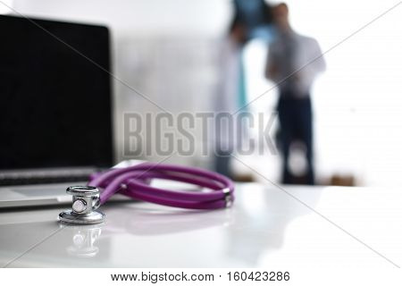 Laptop and stethoscope on the desk doctors standing in the background.