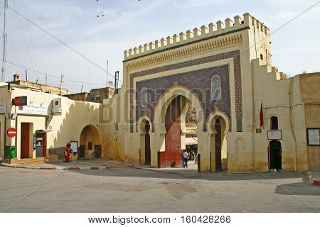 FEZ MOROCCO - MAY 19 2006: Pedestrians walk through the Bab Bou Jeloud (or Blue Gate) the main entrance into the old medina Fes el Bali in Fez Morocco. The Moorish-style gate was built in 1913.