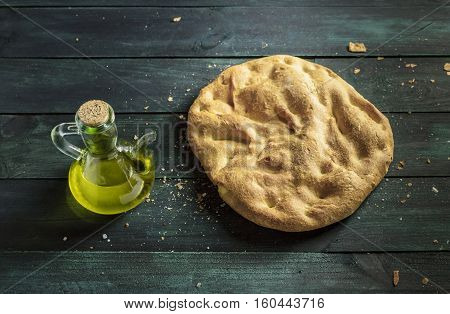 A candid photo of a torta de Aranda, traditional Spanish bread, on a wooden board, with a pitcher of olive oil and copyspace