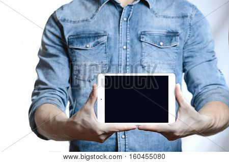 Casual man in denim shirt showing digital tablet computer screen in hands. Isolated on white. Clipping path for display included. He points a finger at the display.