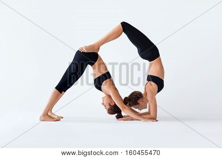 Two Young Women Doing Partner Yoga Asana Down Dog And Scorpion