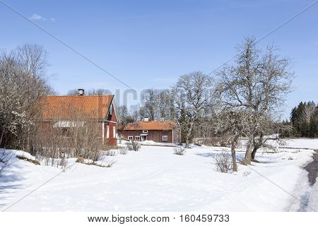 UPLAND, SWEDEN ON APRIL 10. View of a garden and some red wooden buildings on the countryside on April 10, 2013 in Upland, Sweden. Sunny day in spring, snow. Editorial use.