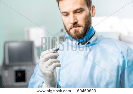 Surgeon holding small surgical scissors for eye operation in the operating room. Image with small deph of field focused on hands and scissors