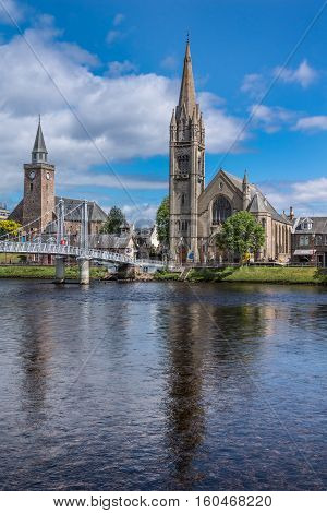 Inverness Scotland - June 1 2012: Combination photo of the Old High Church on the left and the Free Church of Scotland behind the Ness River with part of metallic Greig Street suspension bridge under blue sky.