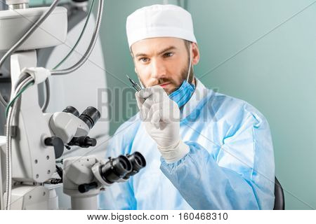 Eye surgeon holding small surgical scissors for eye operation in the operating room near the microscope. Image with small deph of field focused on hands and scissors