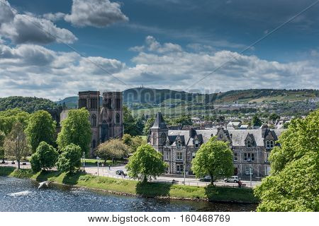 Inverness Scotland - June 1 2012: Brown stone Saint Andrews Cathedral is small in this wide shot of surrounding hills Ness River and other buildings. Shot off Castle Hill. Blue sky with white clouds