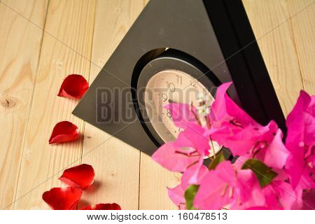 Clock with bougainvillea and rose on wood background.