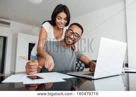 Loving young couple using laptop and analyzing their finances. Writing notes.