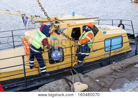 MOSCOW, RUSSIA - NOVEMBER 11, 2016: State Unitary Enterprise Mosvodostok performs recovery vessels on coastal winter parking. Two workers slingers hooked to the vehicle chain slings.