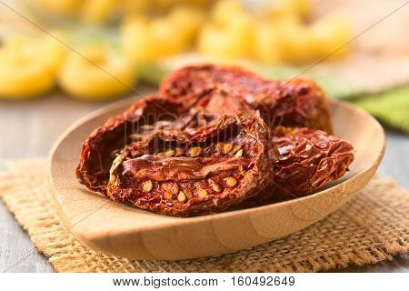 Sun-dried tomato halves on bamboo plate with raw pasta in the back photographed with natural light (Selective Focus Focus in the middle of the first tomato half)