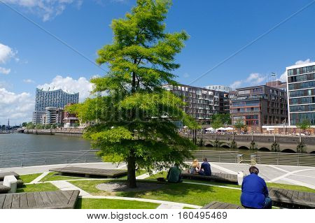 HAMBURG GERMANY - JUNE 18 2015: a little park with trees and resting peoples on beanches on the waterside