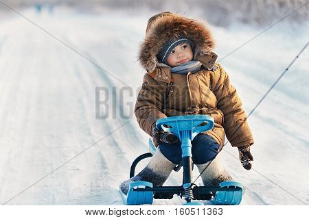 Little boy riding his kids snowmobile winter snow-covered road in the cold