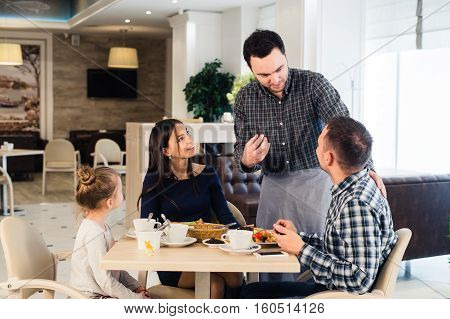 Friendly smiling waiter taking order at table of family having dinner together.