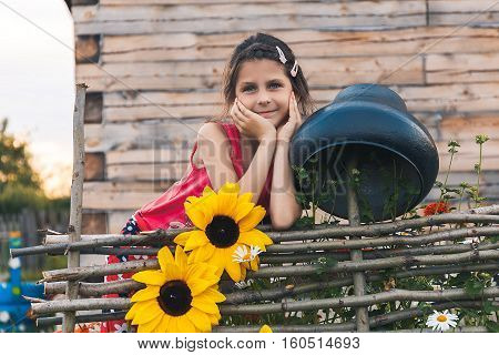 girl leaned on the fence next braided with flowers and a large cast-iron cauldron