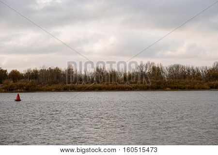 River Bank forest and rippled water surface with river beaconon foreground in bad weather day.