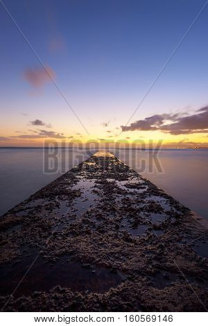Long exposure of pier extending to horizon at a golden hour sunset