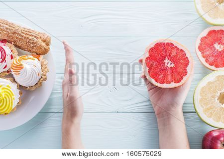Hands of a young woman holding a grapefruit. Woman making a choice between sweets and fruits made a choice in favor of fruits and holding half a grapefruit. Unhealthy vs healthy food top view.
