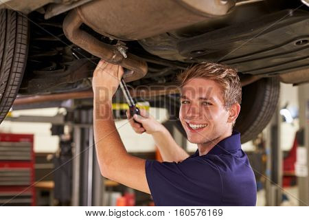 Portrait Of Auto Mechanic Working Underneath Car In Garage