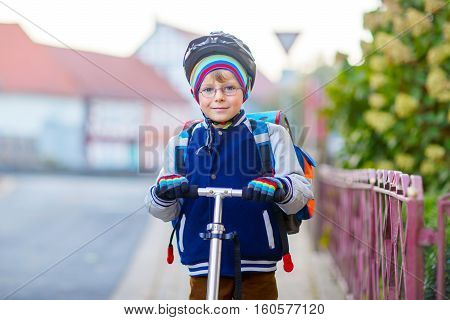 Active school kid boy in safety helmet riding with his scooter in the city. Happy child in colorful clothes biking on way to school. Safe way for kids outdoors to school.