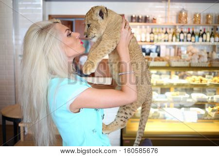 Beautiful woman kisses funny little calf of lion near showcase in cafe