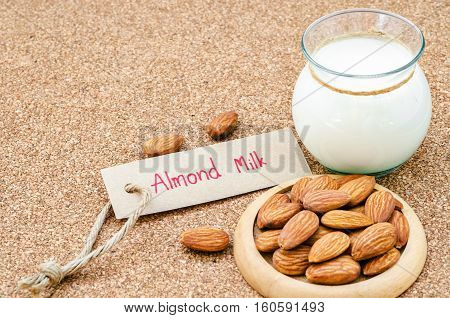 Almond and almond milk in glass with almond tag on wood background.