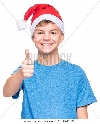 Half-length portrait of caucasian teen boy wearing Santa Claus hat. Teenager looking at camera and making thumb up gesture. Holiday Christmas concept - happy cute child isolated on white background.