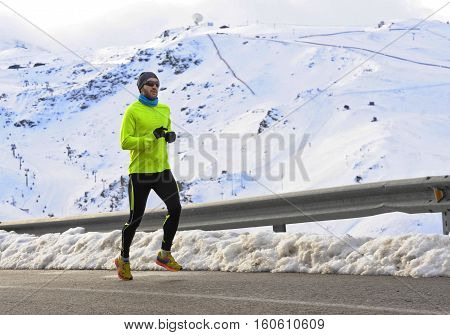 young healthy sport man running on asphalt road at snow mountains in trail runner hard workout in energy and endurance concept with a beautiful cold winter background