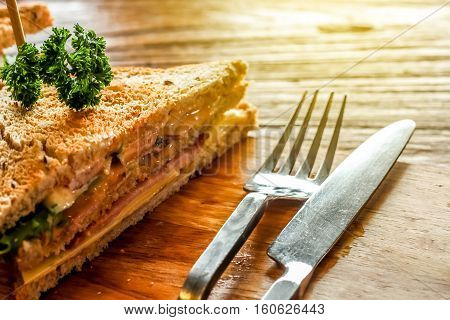 Club sandwich on the wood plate decorate together with fork and knight on the bark wood table background