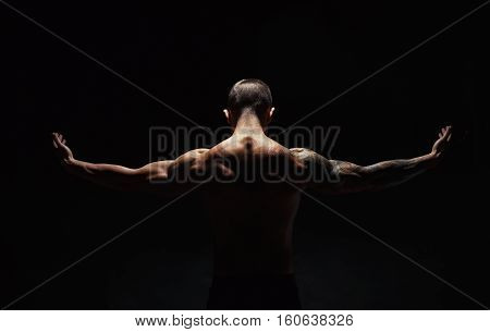 Unrecognizable man bodybuilder shows strong hands and neck muscles, athletic trapezius. Low key, studio shot on black background.