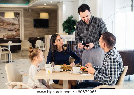 Friendly smiling waiter taking order at table of family having dinner together.