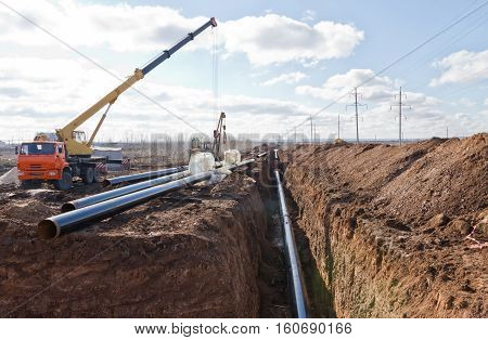 Construction work on the pipe laying of the pipeline into the trench using a crane