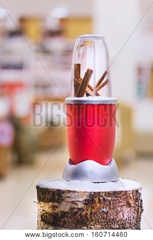 Close view of a red blender with cinnamon sticks on a snowy log Christmas gift.