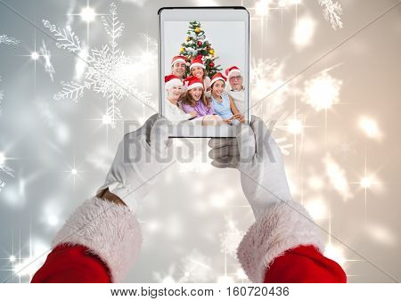 Santa holding a digital tablet with photo of christmas family against digitally generated christmas background