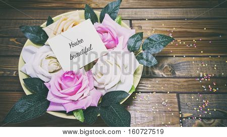 Rose Flowers On A Plate On A Wooden Table, A Note On The Paper