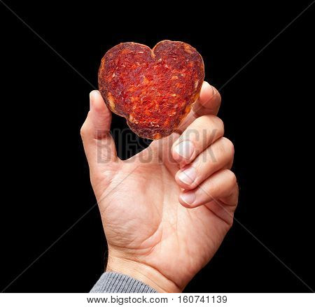 Man hand is holding a heart shape slice of croatian kulen on a black backround.