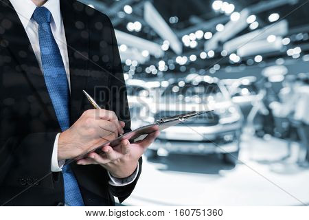 Double exposure of saleman hands holding trade booking with blurred background of new car displayed in showroom dealer buying new car.