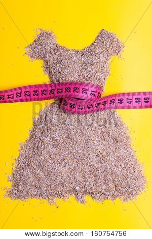 Dieting healthy eating slim down concept. Female dress shape made from cereal bran with measuring tape around thin waistline on yellow