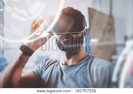 Concept of digital screen, connection and interfaces.Young beraded hipster enjoyingvirtual reality glasses in modern design home studio.Smartphone use with VR goggles headset.Horizontal, flare, blurred