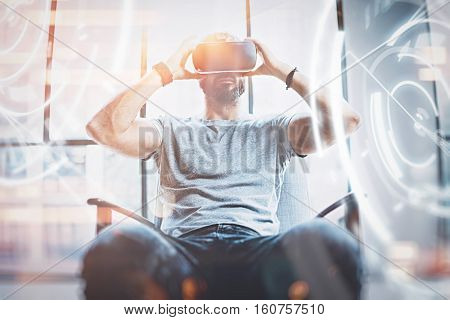 Concept of digital screen, connection and interfaces.Young beraded hipster enjoyingvirtual reality glasses in modern design loft studio.Smartphone use with VR goggles headset.Front view, blurred