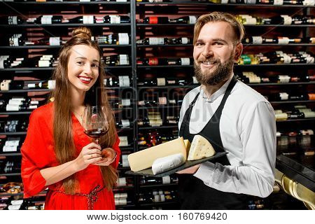 Young woman with glass of wine choosing cheese during the degustation with sommelier or seller at the restaurant or food market