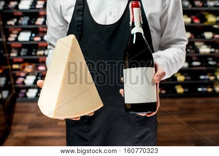 Food seller holding a bottle of white wine and a pieace of parmegiano cheese. Choosing wine according to the type of cheese. Bottle with empty label to copy paste