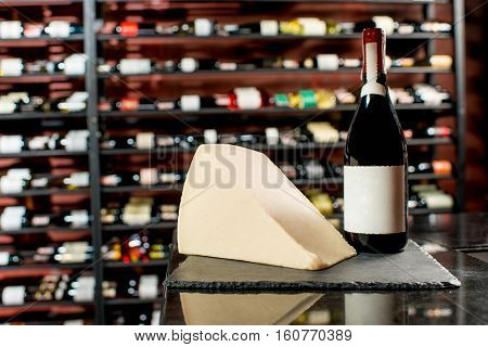 A bottle of wine with a piece of parmegiano cheese on the black board in supermarket or restaurant . Bottle with empty label to copy paste