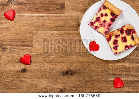 Raspberry cake on white plate and red hearts on wooden background. Valentines Day background