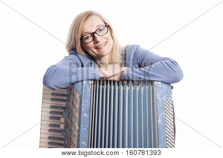 blond woman in blue with glasses leans on accordeon and smiles in studio with white background