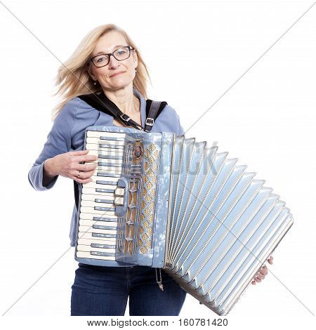 blond woman in blue with glasses plays the accordeon and smiles in studio with white background