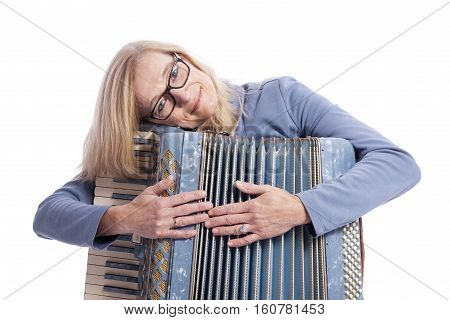 blond woman in blue with glasses holds accordeon and smiles in studio with white background