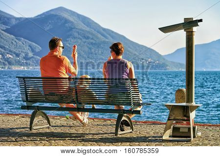 Ascona Switzerland - August 23 2016: Couple eating ice-cream and sitting on the bench at the embankment of the expensive resort in Ascona on Lake Maggiore Ticino canton Switzerland.